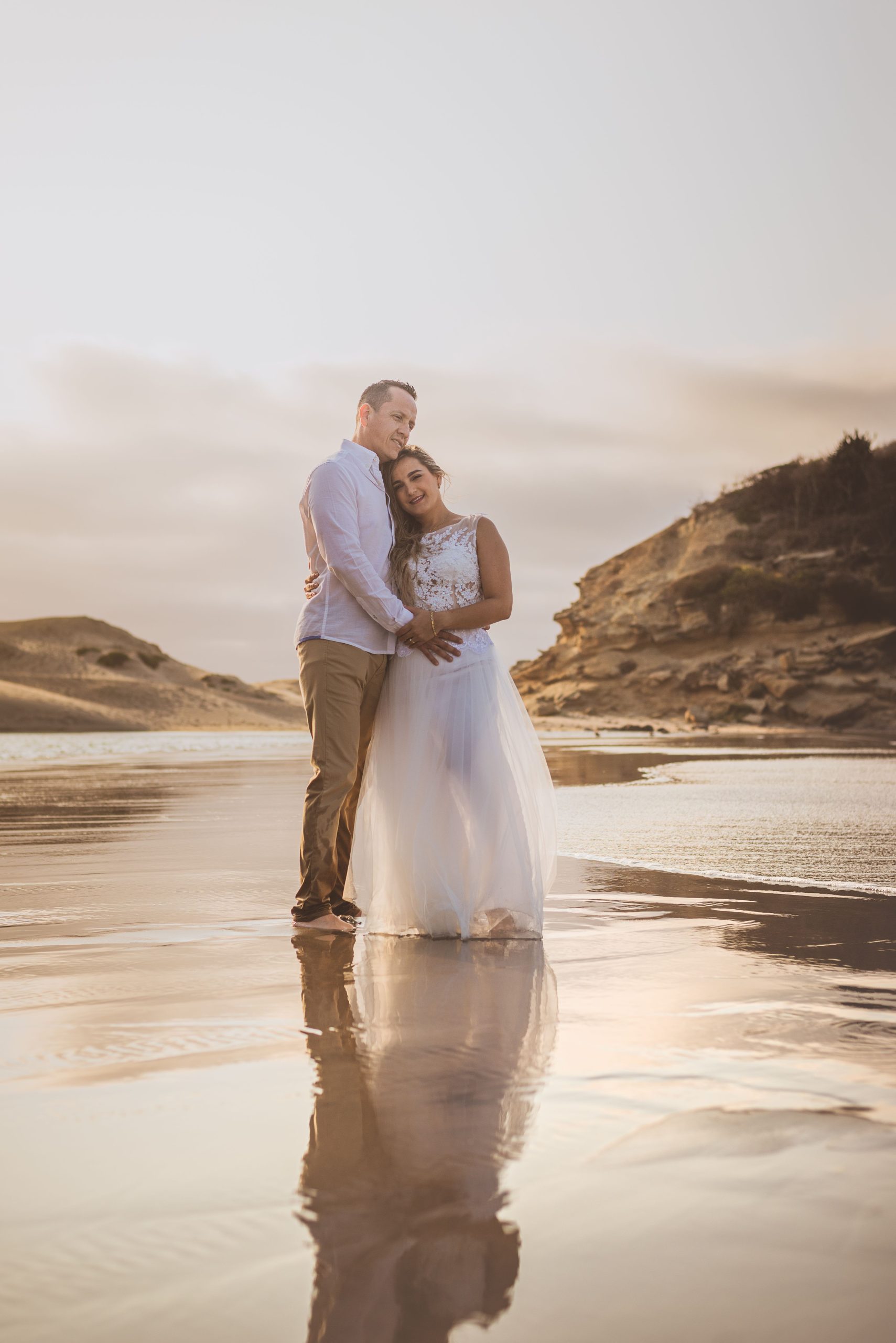 Couple embracing barefoot on the beach at sunset, candid and intimate coastal wedding moment