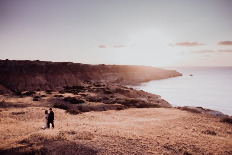 Couple sharing a romantic elopement moment at sunset on an Australian beach, warm golden light