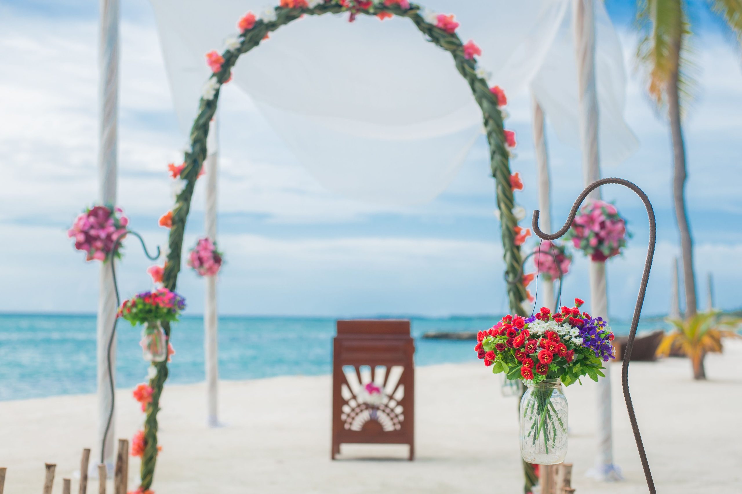 Intimate beach wedding ceremony setup with a floral arch and ocean backdrop on the sand