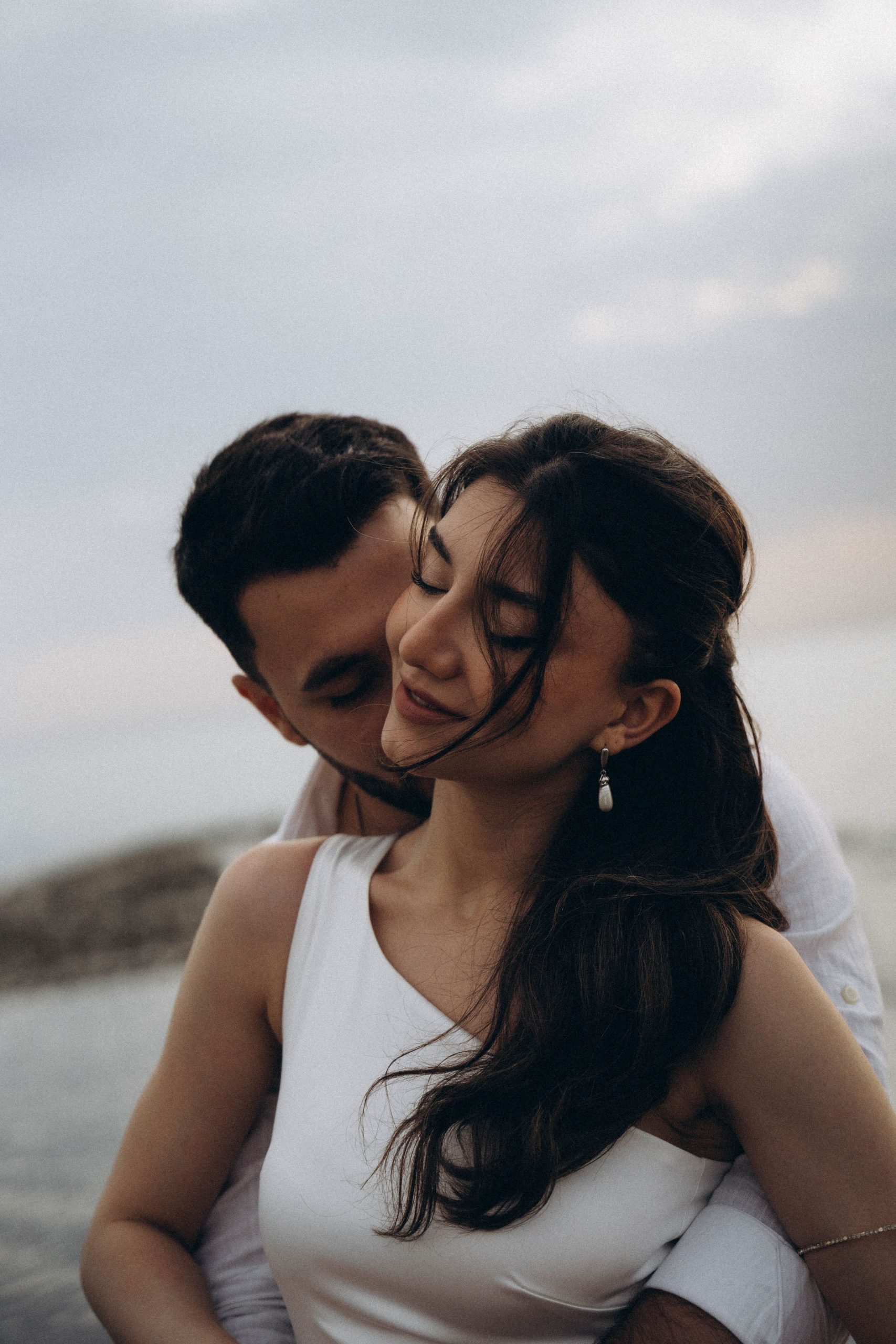 Newlywed couple sharing an intimate barefoot moment on the beach at dawn, candid golden light